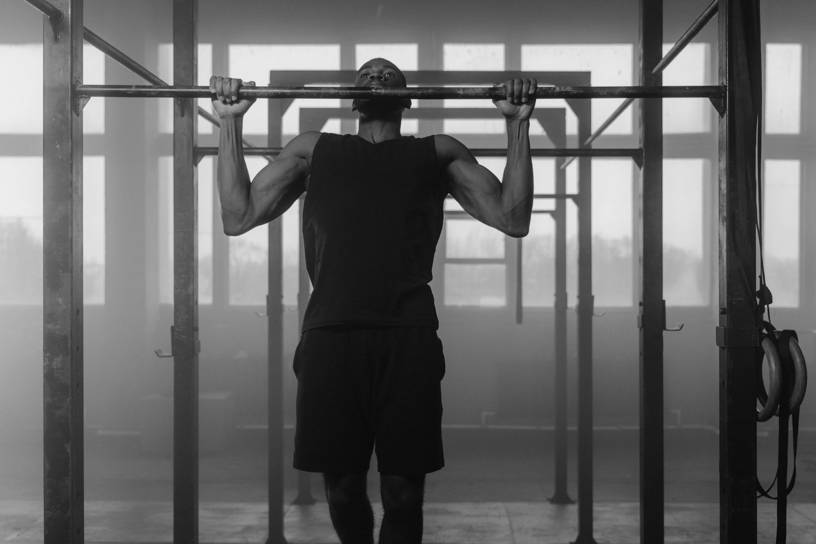 Un hombre hace dominadas en un gimnasio, en blanco y negro.